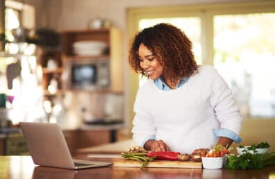 A woman cooking while looking over a recipe.