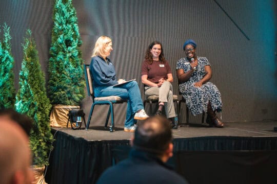 Sound employee, Jen Reed, and members of Emergency Food Network sitting on stage.