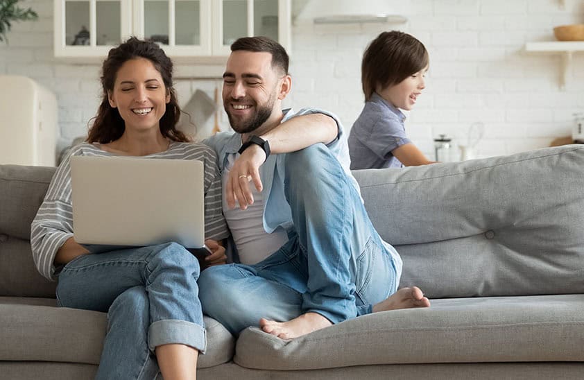 Husband and wife using laptop while you boy plays in the background.