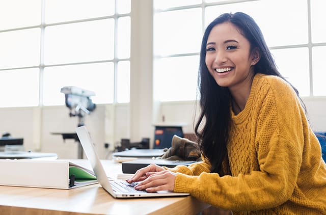 A student smiling while working on their laptop.
