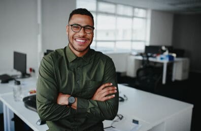 A professional man standing in front of a desk with arms crossed.