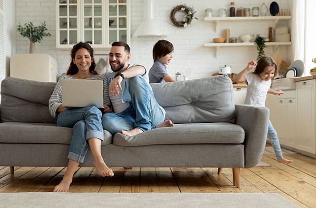 While active kids running parents resting on sofa using laptop