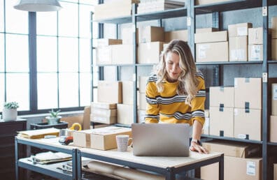 A woman running an online business while standing next to boxes.
