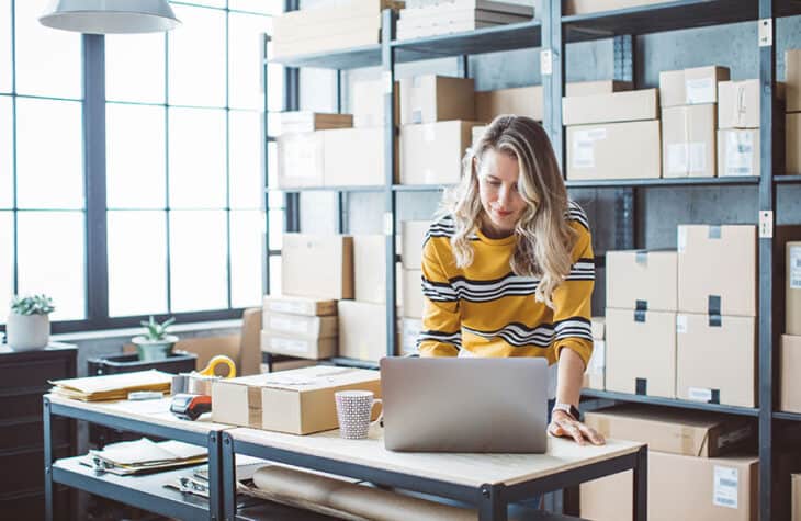A woman running an online business while standing next to boxes.