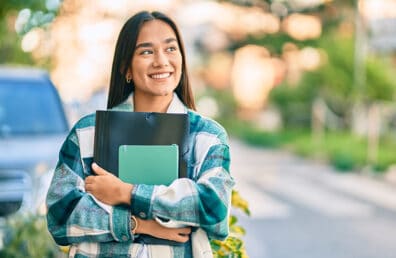 A female student walking while holding her books.