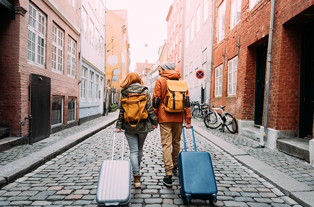 couple dragging suitcases up a cobblestone road abroad