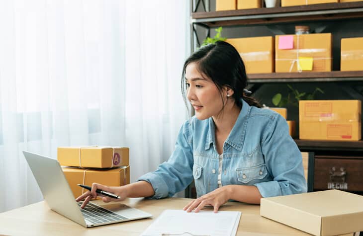 A small business owner looking at paperwork on her laptop.