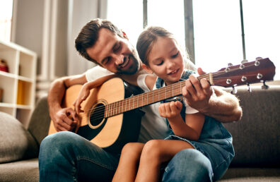 father teaching daughter how to play guitar