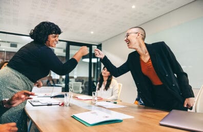 Two cheery business women fist bumping.