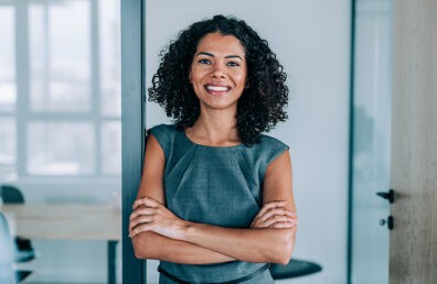 A confident woman smiling at the camera with arms crossed.