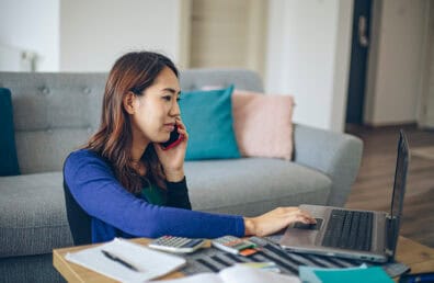 A woman working on financial documents while taking a phone call.