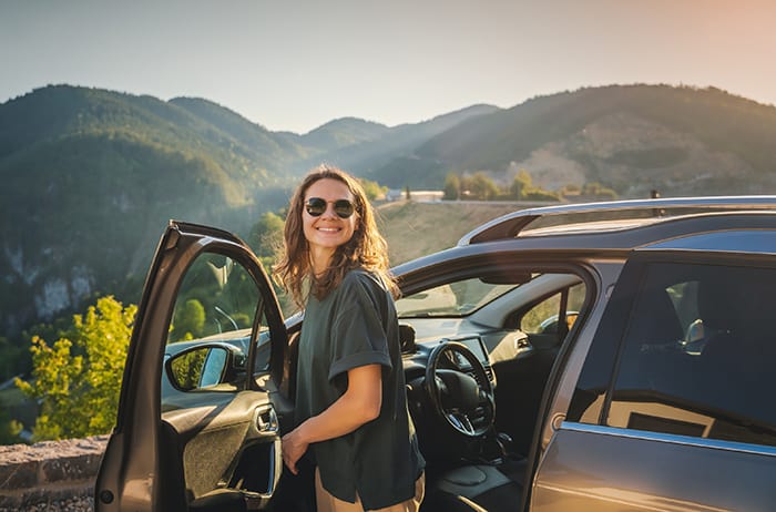 A women standing happily outside of her car.