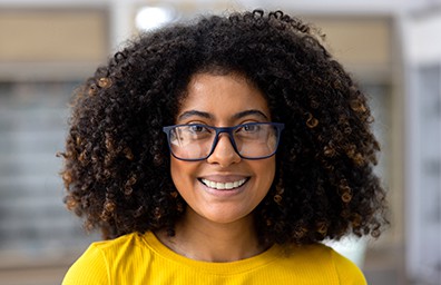 Student in yellow top and blue glasses looking at camera