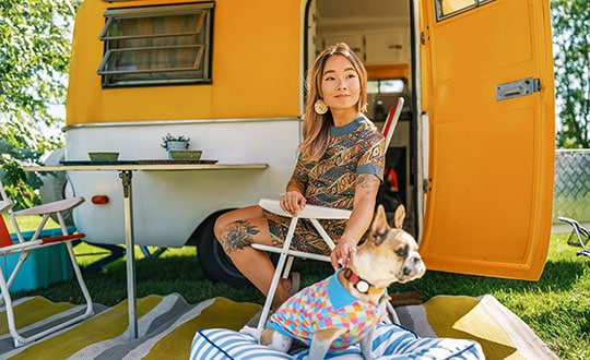 A young woman sitting with her dog while seated outside of a camper vehicle.