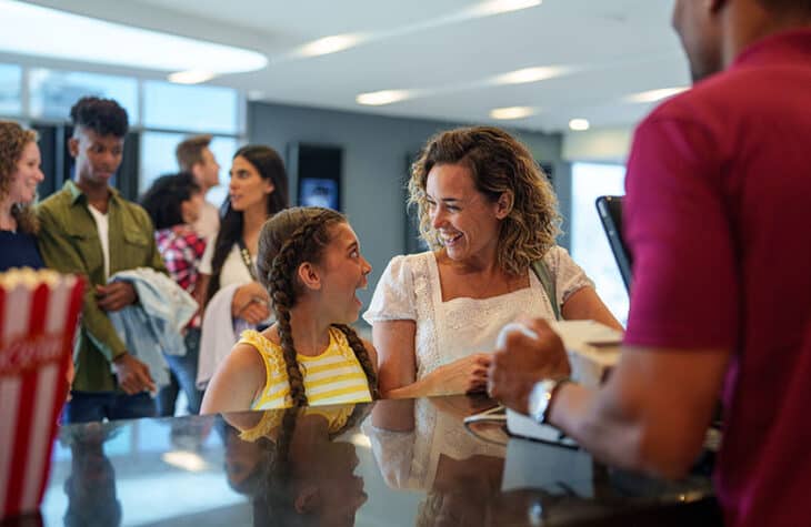 Mother and daughter cheerfully buying movie tickets at movie theater box office