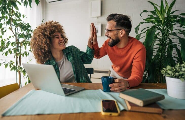 Two workmates excited about new job success. High five. Man and woman, colleagues, sitting at the table and working together using laptop.