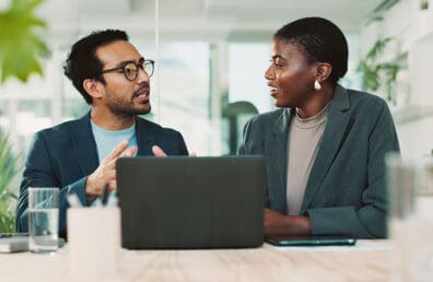 Two working professional having a conversation behind a laptop.