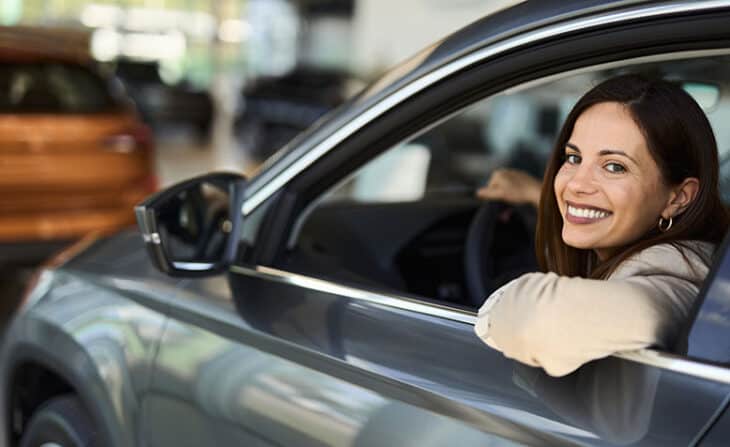 Happy woman buying new car in a showroom