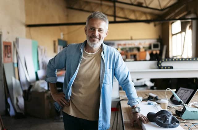 Portrait of a mature engineer smiling in his workshop, posing next to his 3d printer