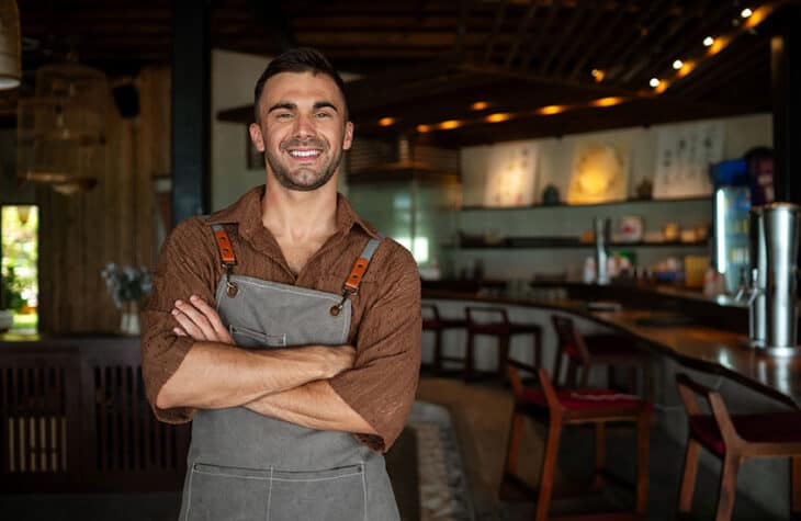 Male business owner standing in his cafe with arms folded.