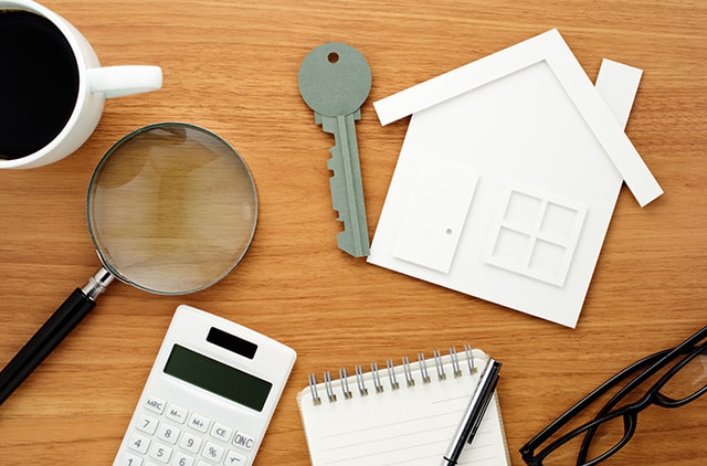 House and key shaped paper cutout plus calculator and magnifier on wooden table