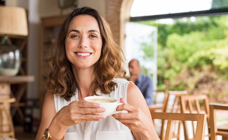 Woman holding cappuccino in modern cafe smiling at camera