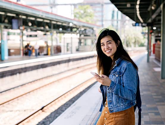 Student traveler on the go at a train station doing mobile banking with their smart phone