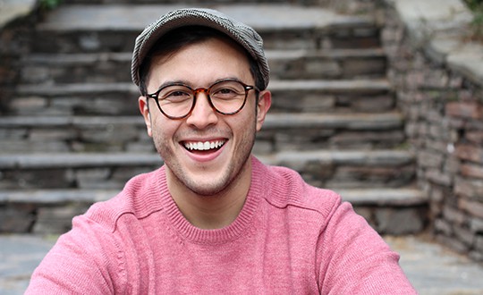 hip man wearing a newsboy hat smiling outside near concrete steps