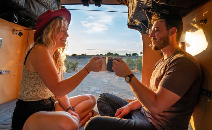 young couple camping in their vehicle and clinking their coffee mugs together